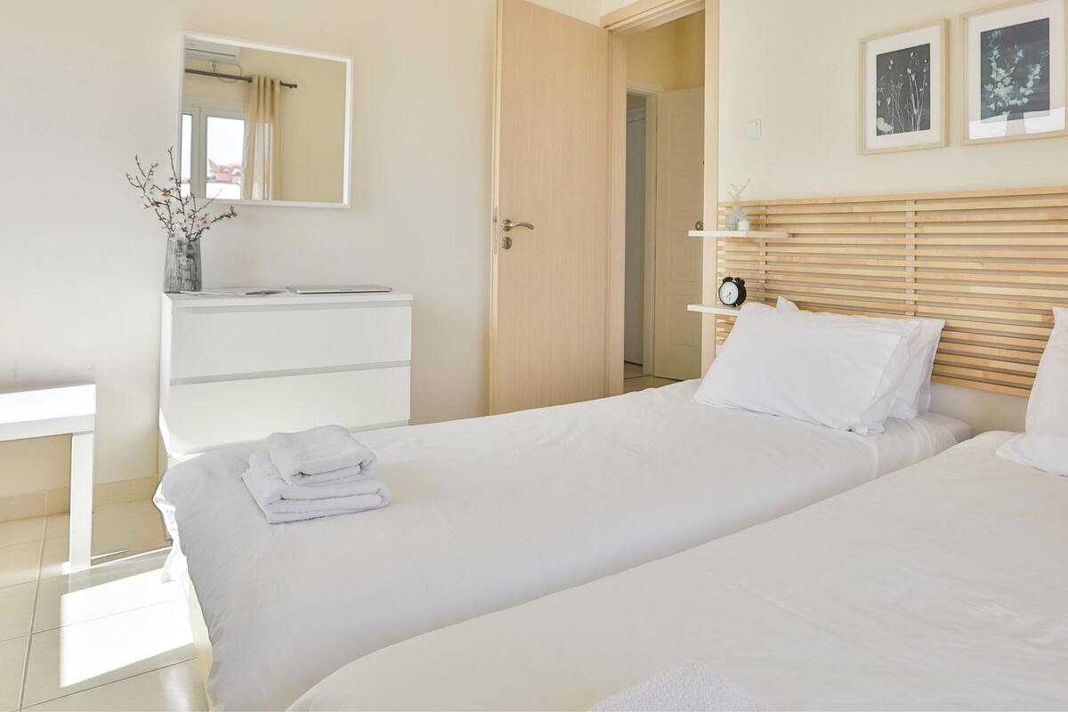 A hotel room with two beds, a white dresser, a mirror, and framed artwork on the wall.
