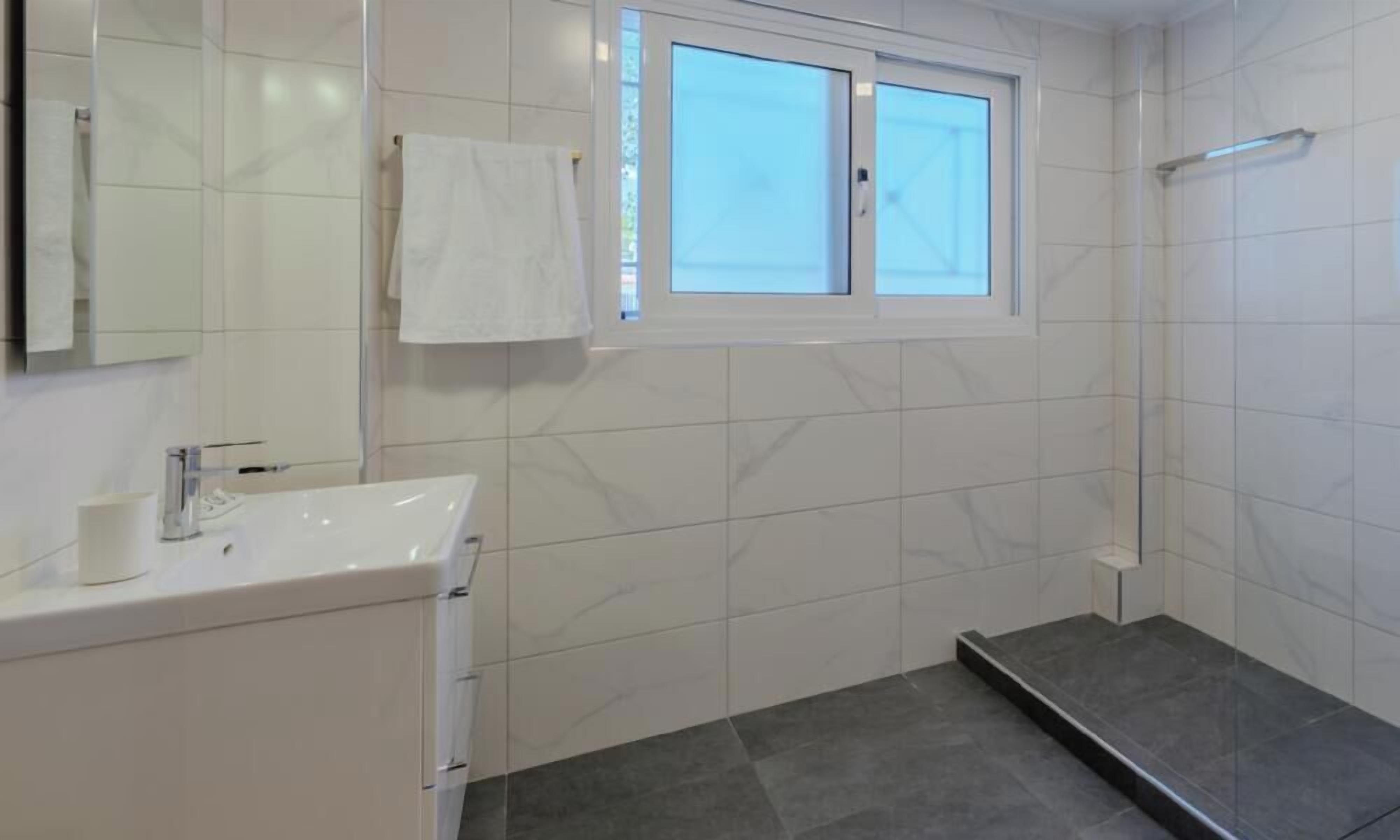 A bathroom with a white sink, a mirror, a towel hanging on the wall, and a shower area.