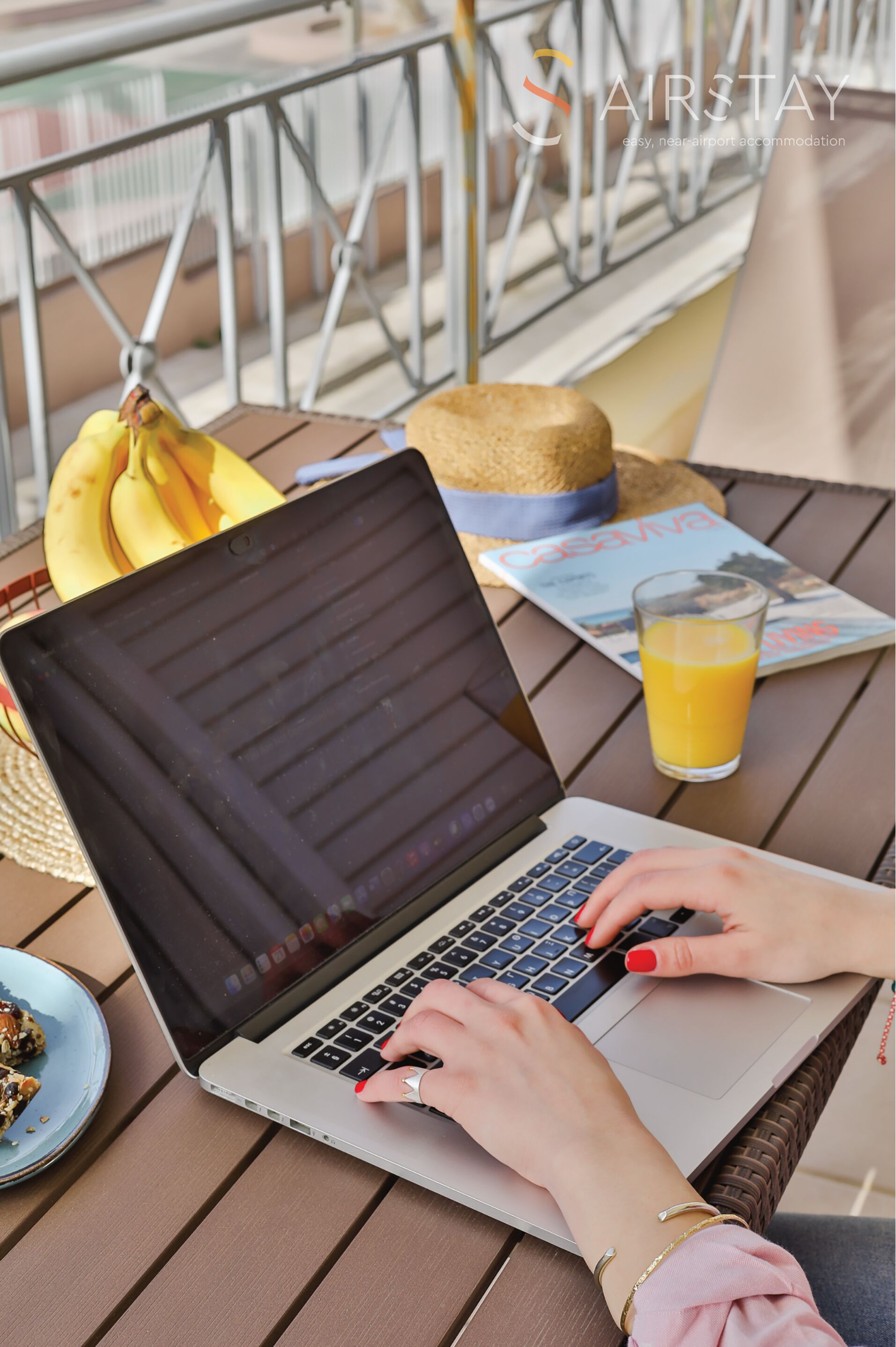 Un ordinateur portable est posé sur une table, à côté d’un magazine, d’un verre de jus d’orange et d’une paille.
