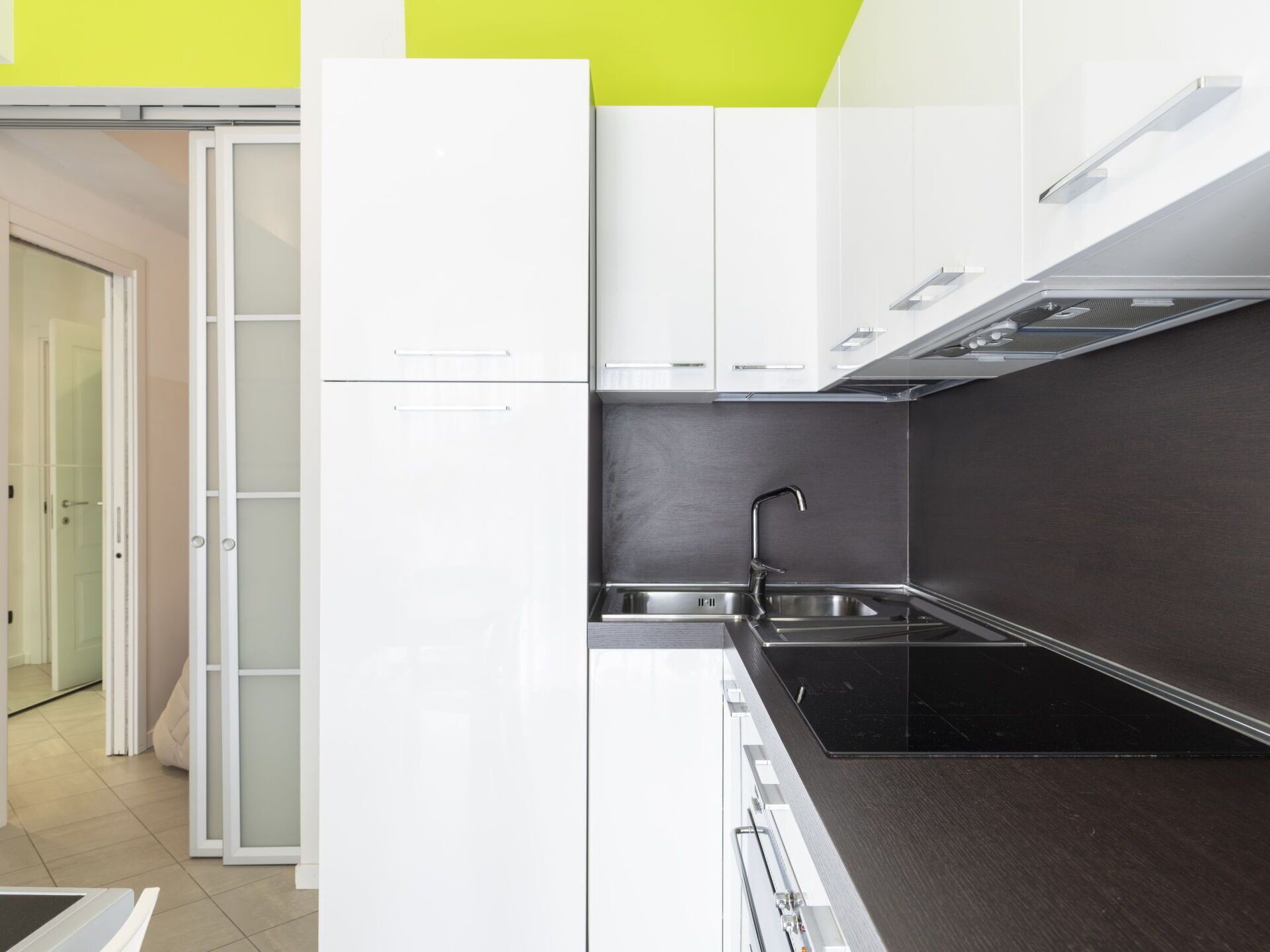 Une cuisine moderne avec des meubles blancs, un plan de travail noir et un évier en acier inoxydable.