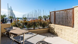 Eine Terrasse mit Blick auf einen Hafen, Sitzgelegenheiten im Freien und eine Steinsäule.