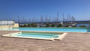 Ein Schwimmbecken mit Holzterrasse, umgeben von einer Marina mit zahlreichen Booten.