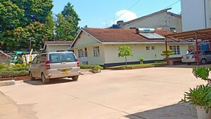 A parking area with several cars, a building with a tiled roof, and potted plants. - St. Anna Guest House (Kisumu)