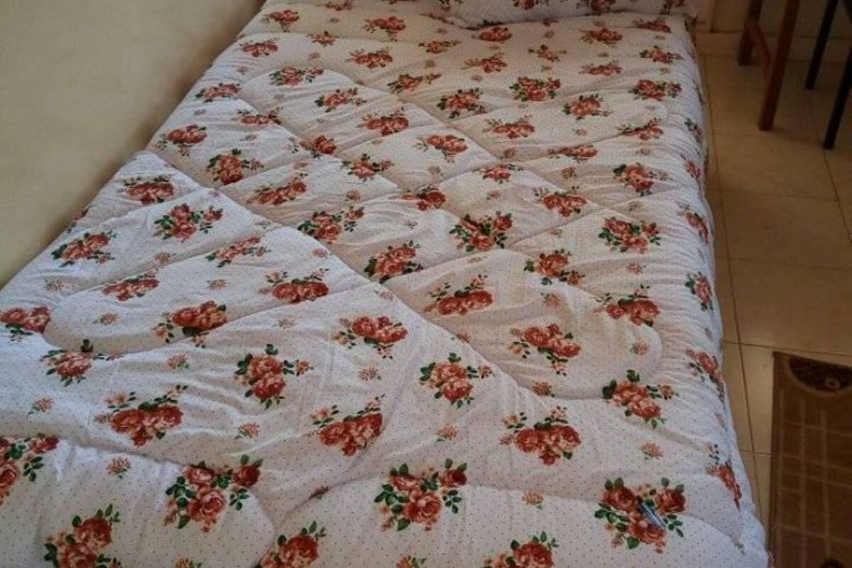Una cama con colcha estampada y almohadas a juego en una habitación con ventana y una silla.
