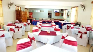 A banquet hall with round tables covered in white tablecloths and red sashes, arranged for a formal event. - St. Anna Guest House (Kisumu)