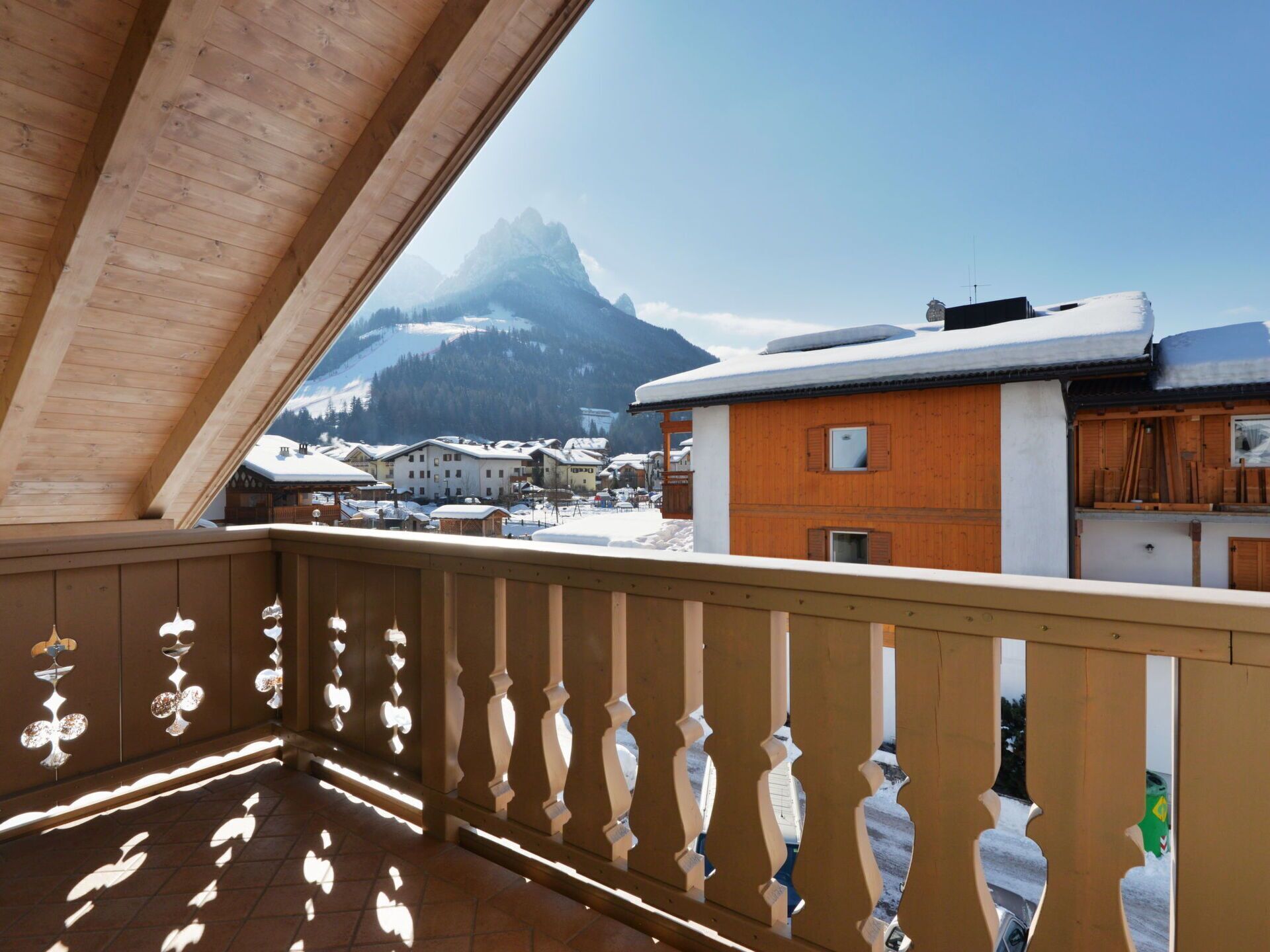 Un balcón de madera con vistas a una montaña y edificios cubiertos de nieve.