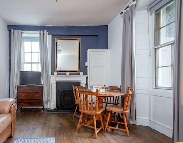 A room with a fireplace, a dining table with chairs, a television, and a large mirror.