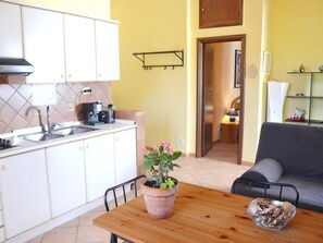 Une cuisine de taille réduite avec des meubles blancs, une machine à café et une plante en pot posée sur le plan de travail.