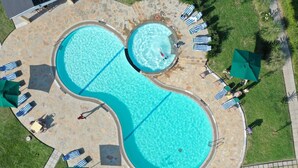 Una piscina circular con dos zonas separadas, rodeada de sillones de descanso y sombrillas.