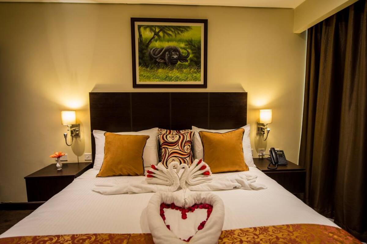 A hotel room with a large bed, two nightstands, a framed picture on the wall, and a heart-shaped towel on the bed.