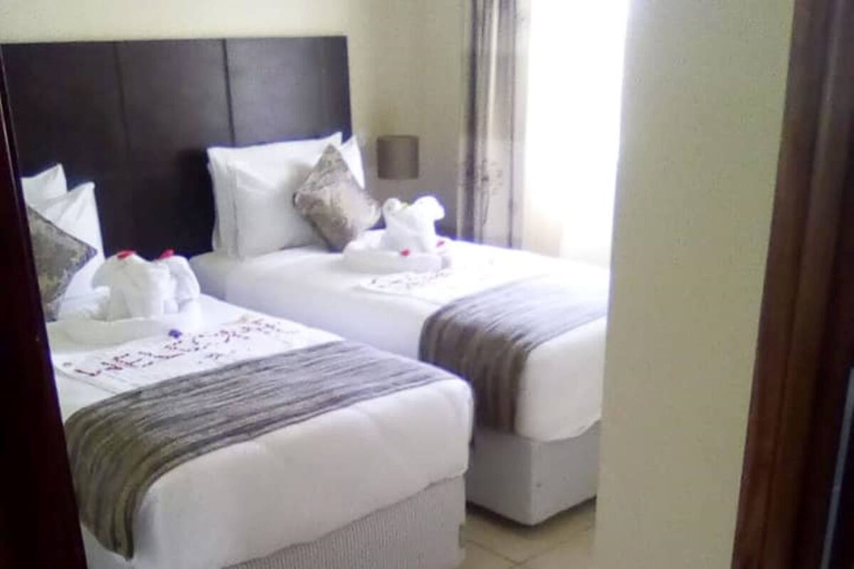 A hotel room with two beds, a headboard, a bedside table, and a window with curtains.