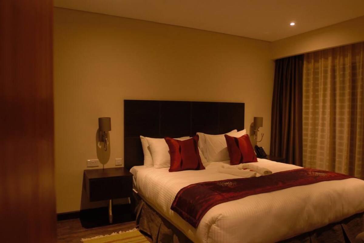 A hotel room with a large bed, a dark headboard, two bedside tables, and a red throw blanket.