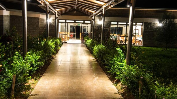 Un paseo techado que conduce a un edificio con puertas de cristal y un patio con mesas y sillas.