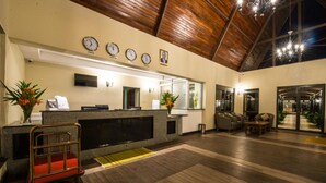 Zona de recepción de hotel con techo de madera, mostrador de recepción, área de estar y vista al exterior.