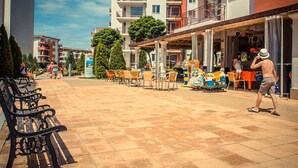 Un espace extérieur ensoleillé avec un café, des tables et chaises à l’extérieur, et un petit train pour faire le tour.