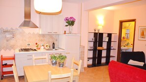 A compact kitchen with white cabinets, a dining table with chairs, a red chair, and a vase with flowers. - Apartment "B" in cottage with garden, parking and Wi-Fi (Ercolano)