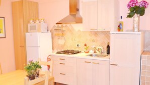 A compact kitchen with white cabinets, a gas stove, a microwave, and a sink. There is a dining table with chairs and a potted plant. - Apartment "B" in cottage with garden, parking and Wi-Fi (Ercolano)