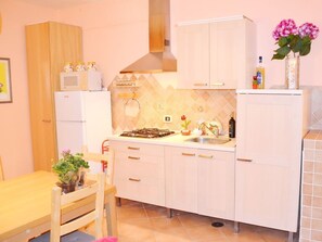 A compact kitchen with white cabinets, a gas stove, a microwave, and a sink. There is a dining table with chairs and a potted plant.