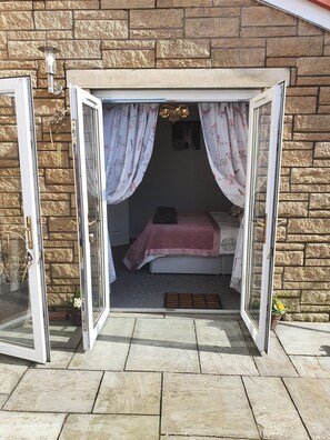 Une chambre ouverte comprenant un lit, une fenêtre avec des rideaux, un petit tapis et un luminaire fixé au mur.