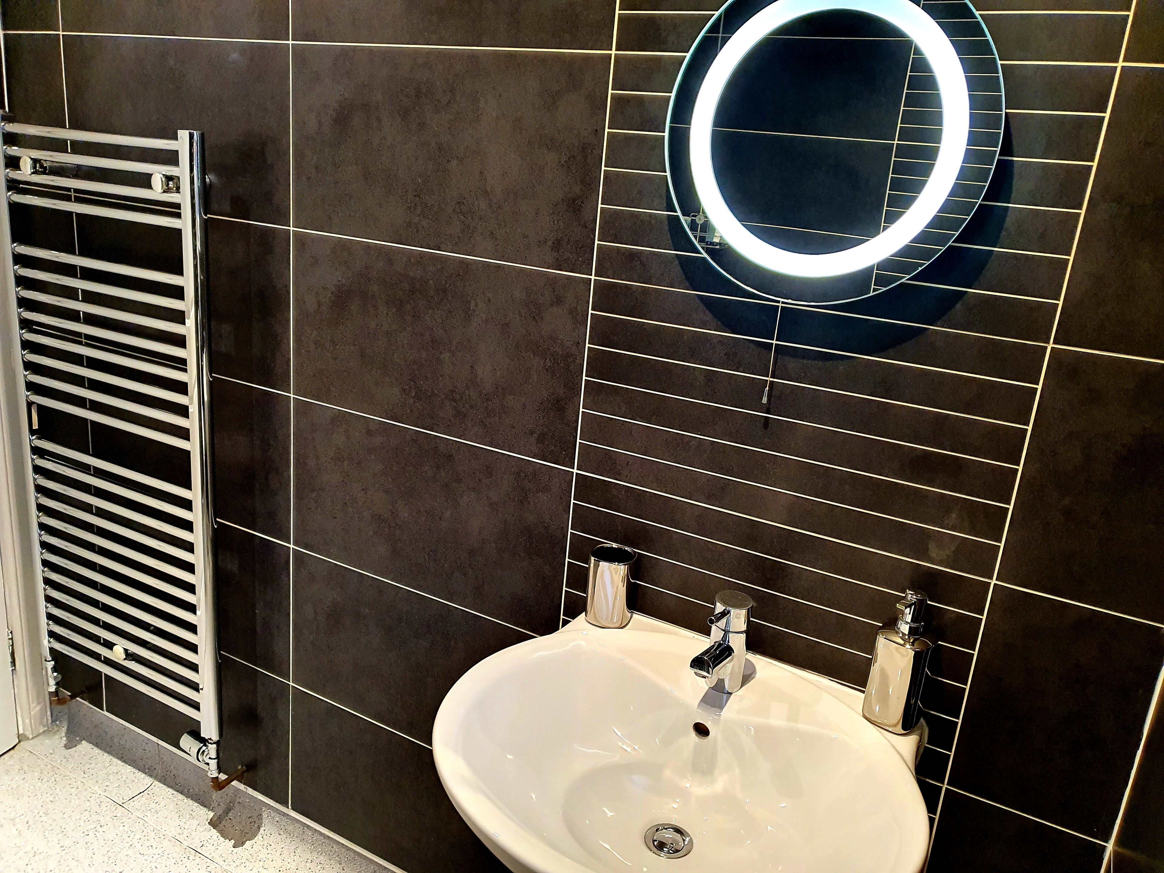 A bathroom with a white sink, a mirror with a circular light, and a towel rack.