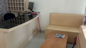 A small, compact room with a wooden desk, a computer, a cushioned bench, and a small wooden table. - Sunvasha Hotel (Naivasha)