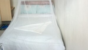 A single bed with a mosquito net, a wooden shelf, and a plain wall. - Sunvasha Hotel (Naivasha)