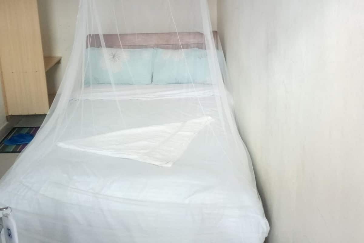 Uma cama de solteiro com mosquiteiro, uma prateleira de madeira e uma parede lisa.