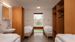 Habitación de hotel con dos camas, una ventana, armario de madera y un lavamanos.