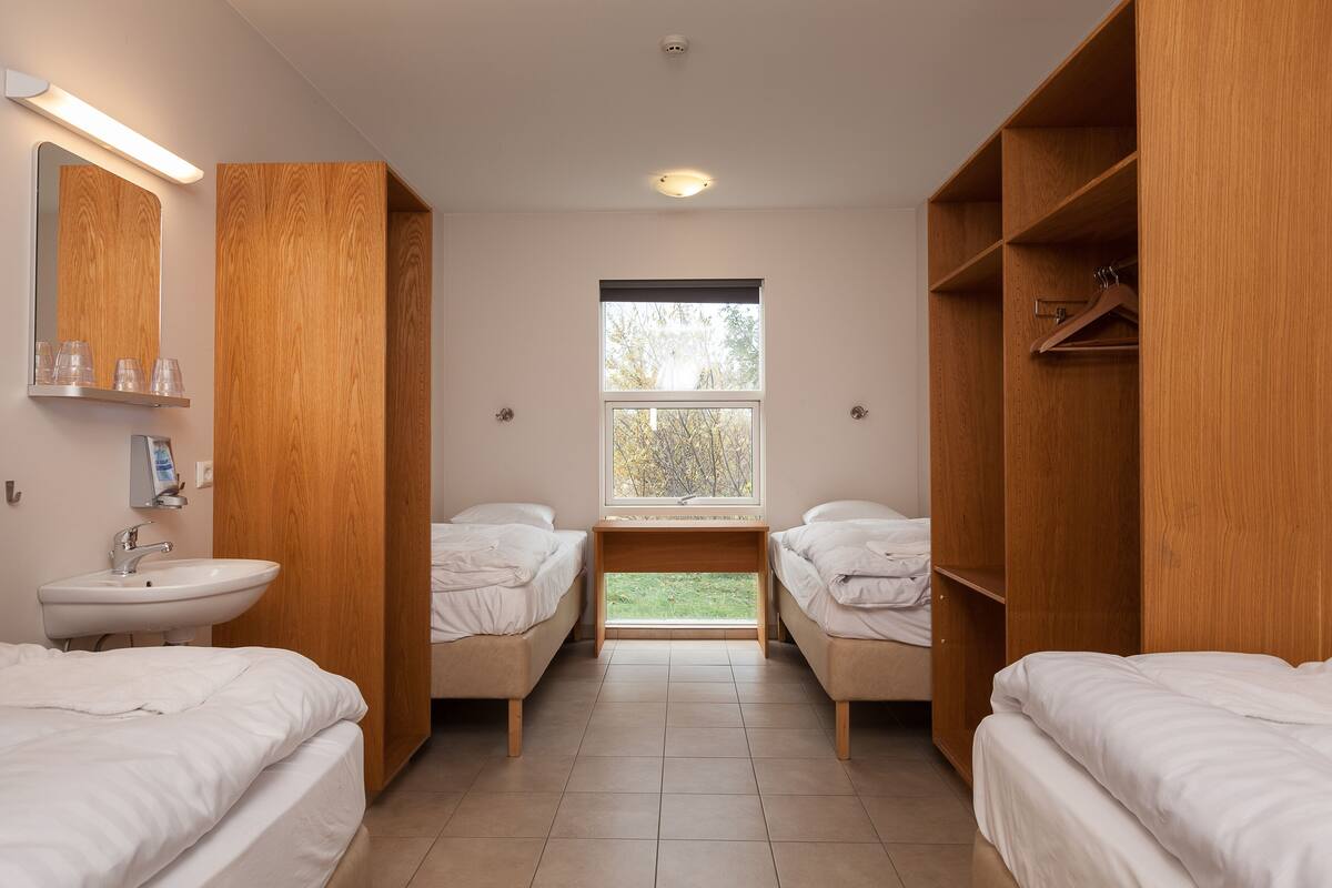 Een hotelkamer met twee bedden, een raam, een houten garderobe en een wastafel.