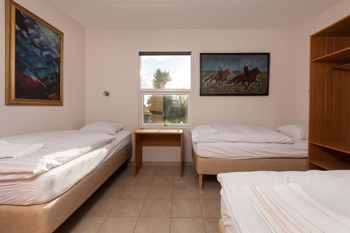 Een kamer met twee eenpersoonsbedden, een houten bureau, een raam en twee schilderijen aan de wand.