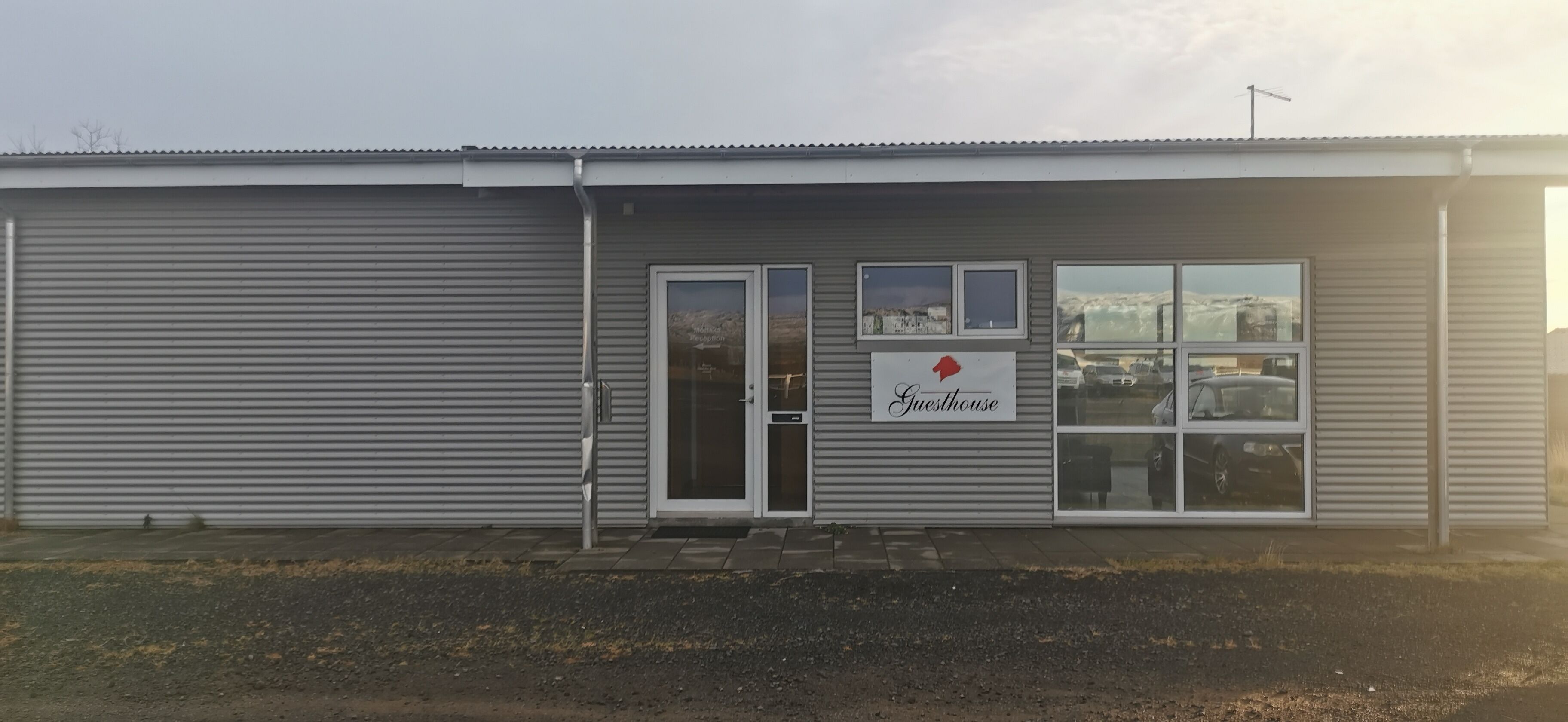 A building with a closed shutter door, a sign reading "Guesthouse," and a window with a view of parked cars.