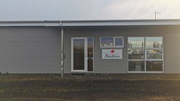 A building with a closed shutter door, a sign reading "Guesthouse," and a window with a view of parked cars.