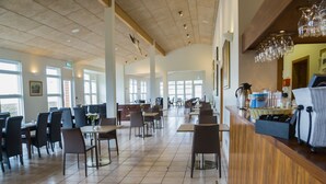 Un restaurante espacioso con techos altos, ventanas amplias y diferentes opciones de asientos, incluyendo mesas y sillas.