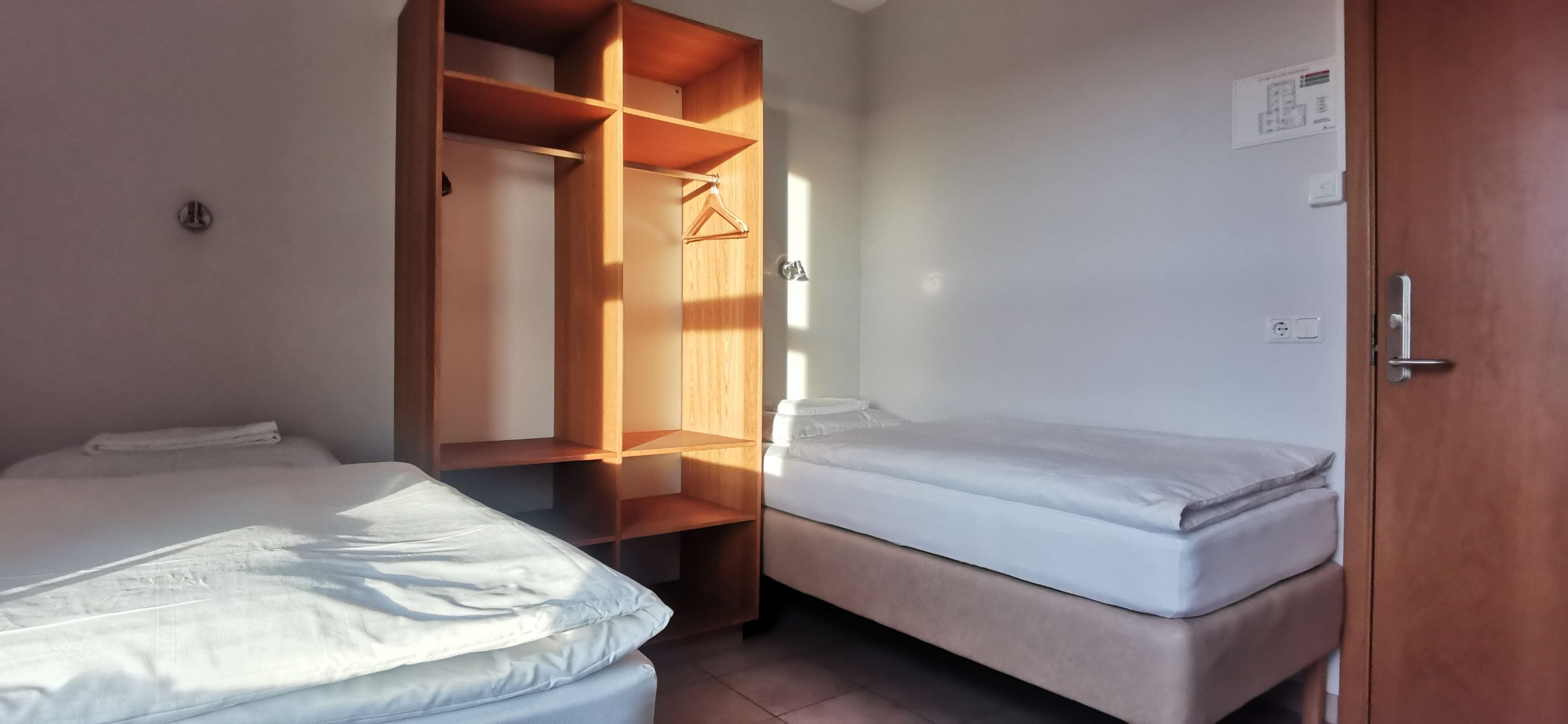 A compact room with two beds, a wooden wardrobe, and a door with a handle.