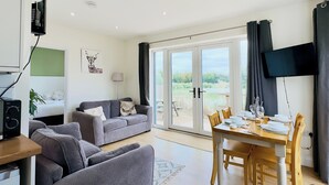 Una sala de estar moderna con un sofá gris, una mesa de comedor preparada para cuatro personas y un amplio ventanal corredero que da a un jardín.