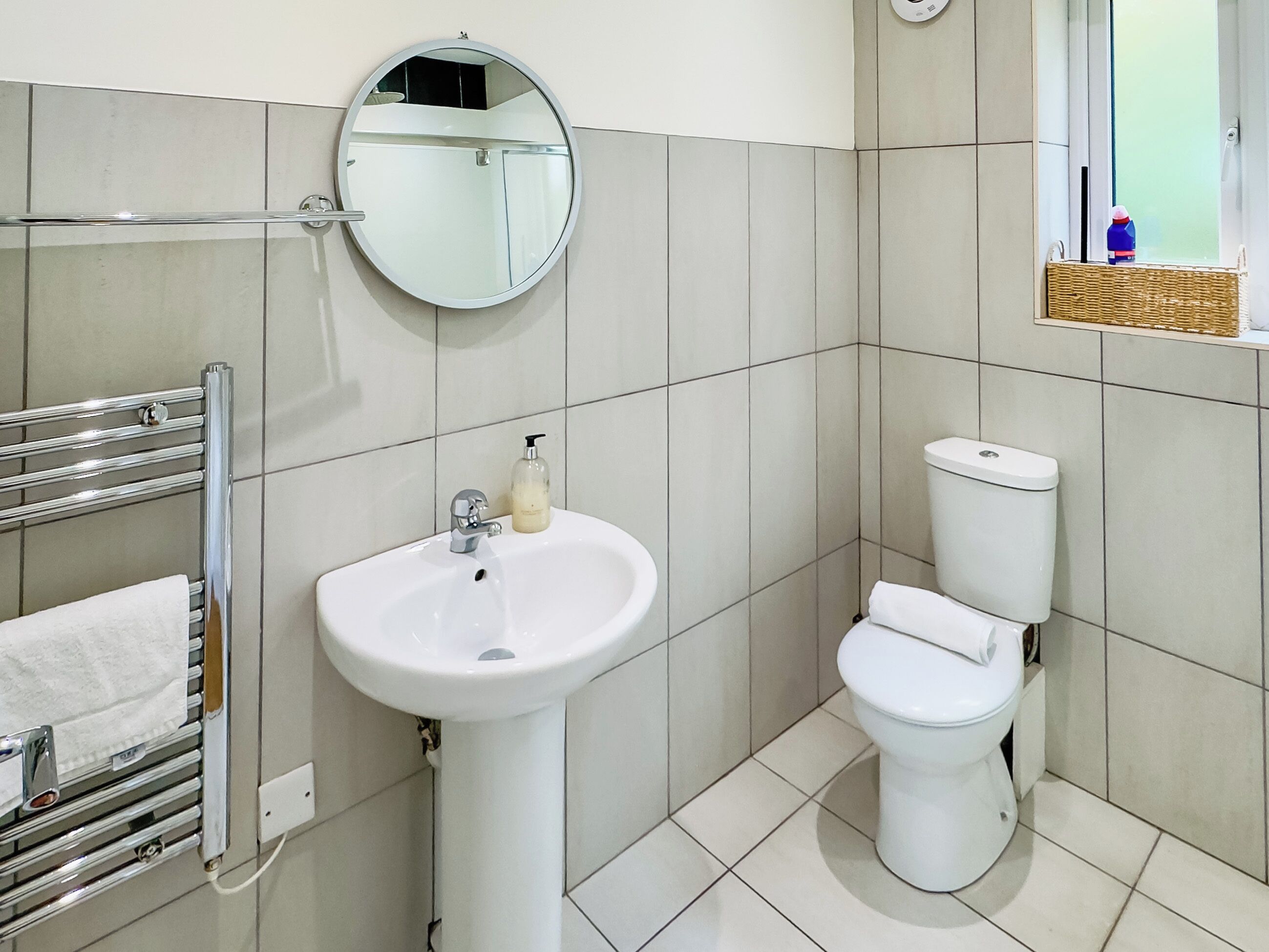 Kylpyhuone, jossa on valkoinen pesuallas, peili, wc-istuin ja pyyheteline.