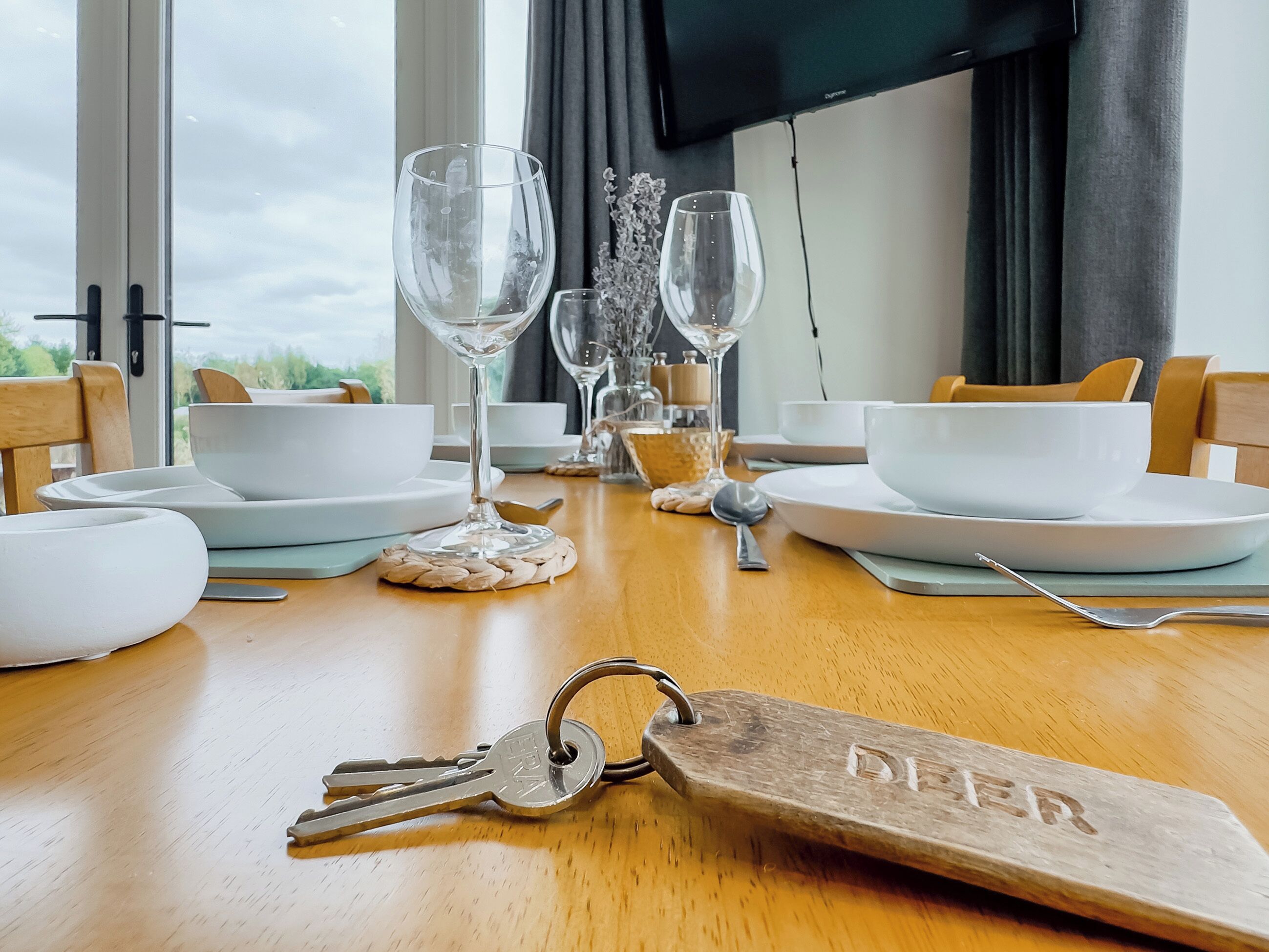Mesa de jantar posta com pratos, tigelas e copos de vinho brancos, com um chaveiro com a etiqueta 