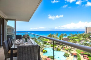 Varanda com mesa de jantar para dois, com vista para a área da piscina do resort, palmeiras e o oceano.
