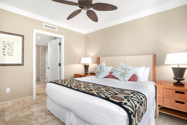 A hotel room with a large bed, two bedside tables with lamps, a ceiling fan, and a door leading to another room.