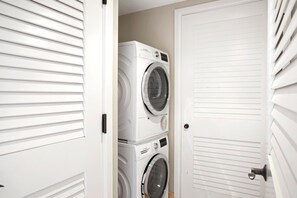 Uma lavanderia com duas máquinas de lavar roupa frontais empilhadas e uma porta fechada.