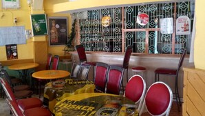 A restaurant with a yellow and black tablecloth-covered table, red chairs, and a window with decorative metal bars. - Sweet Banana House (Lamu)
