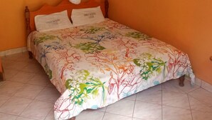 A bedroom with an orange wall, a wooden bed frame, a floral bedspread, and a white canopy. - Sweet Banana House (Lamu)