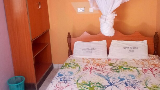 A bedroom with a bed, a wooden wardrobe, a mosquito net, and a trash bin. - Sweet Banana House (Lamu)