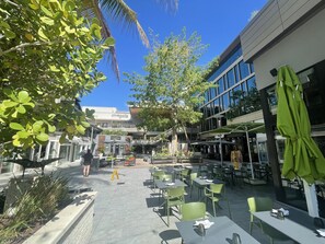 An outdoor cafe area with tables and chairs, a palm tree, and a building with a 'cinepolls' sign. - I. Historic Home Key West style in Coconut Grove Yellow House (Miami)