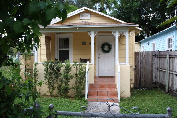 A single-story house with a front porch, a door with a wreath, and a small front yard. - I. Historic Home Key West style in Coconut Grove Yellow House (Miami)