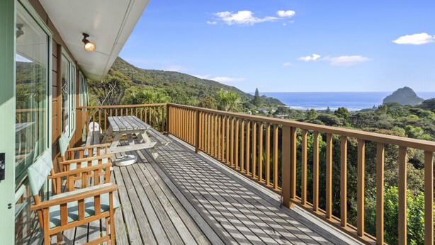 A wooden deck with chairs and a table, overlooking a mountainous landscape and the ocean. - Seaview, Sun and Surf - Piha Holiday Home (Piha)
