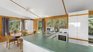 A modern kitchen with wooden accents, a central island, and a dining area with chairs. - Seaview, Sun and Surf - Piha Holiday Home (Piha)