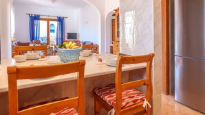 Comedor con encimera de mármol, sillas de madera con cojines estampados y una cesta de fruta.