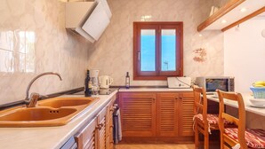 Una cocina con un lavaplatos doble, armarios de madera, un ventanal con vistas, un microondas y una zona de comedor con sillas.