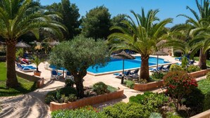 Zona de piscina con sillones de descanso y palmeras.